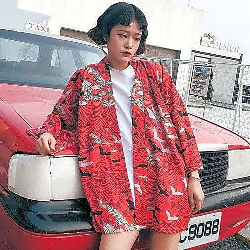 Czerwone krótkie kimono damskie w japoński wzór z lecącymi żurawiami, widok z przodu na modelce opierającej się o samochód.