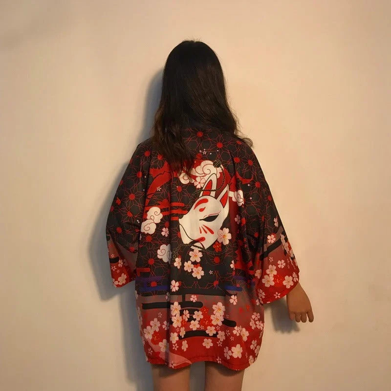 Damska narzutka kimono w japońskim stylu, czerwono-czarna, z motywem maski Kitsune i kwitnącej sakury, widok z tyłu na modelce.