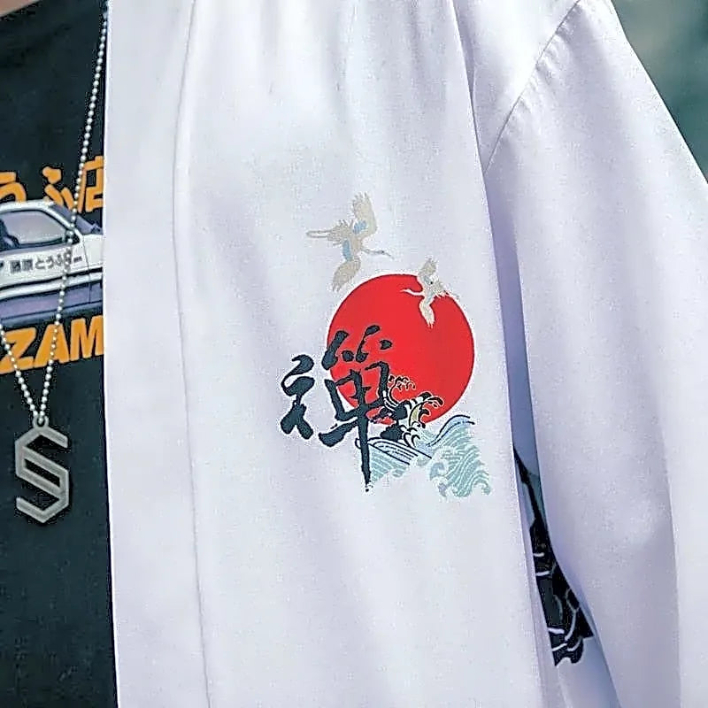 Zbliżenie na detal wzoru na białej narzutce kimono haori: japońska kaligrafia kanji, czerwone słońce, fale i żurawie.