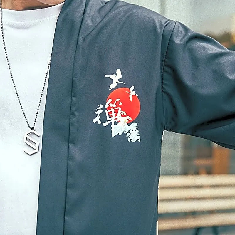 Detal wzoru na piersi czarnej narzutki kimono haori: japońskie znaki, czerwone słońce i fale.