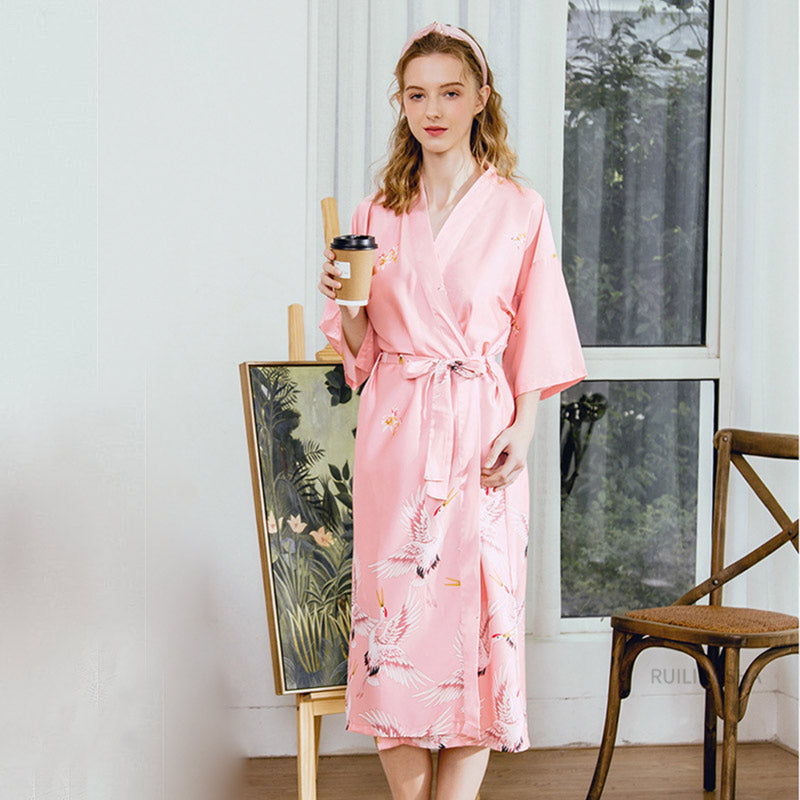 Modelka prezentująca długi różowy szlafrok kimono z motywem żurawi, idealny do relaksu w domu.