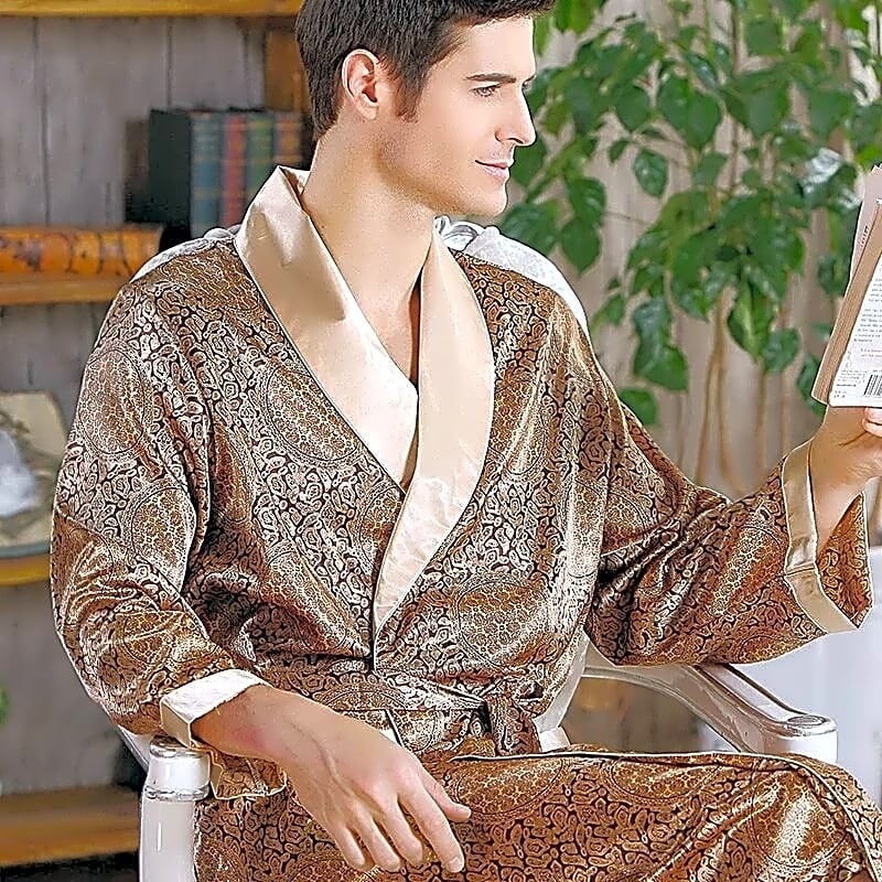 Mężczyzna w eleganckim brązowym szlafroku kimono z satyny we wzór paisley i beżowym kołnierzem, czytający książkę w domowym zaciszu.