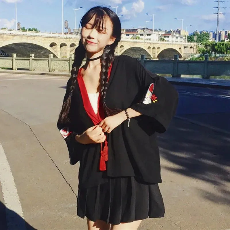 Uśmiechnięta modelka w czarnym kimonie japońskim z czerwonym wykończeniem i motywem lisa kitsune, pozująca na zewnątrz.