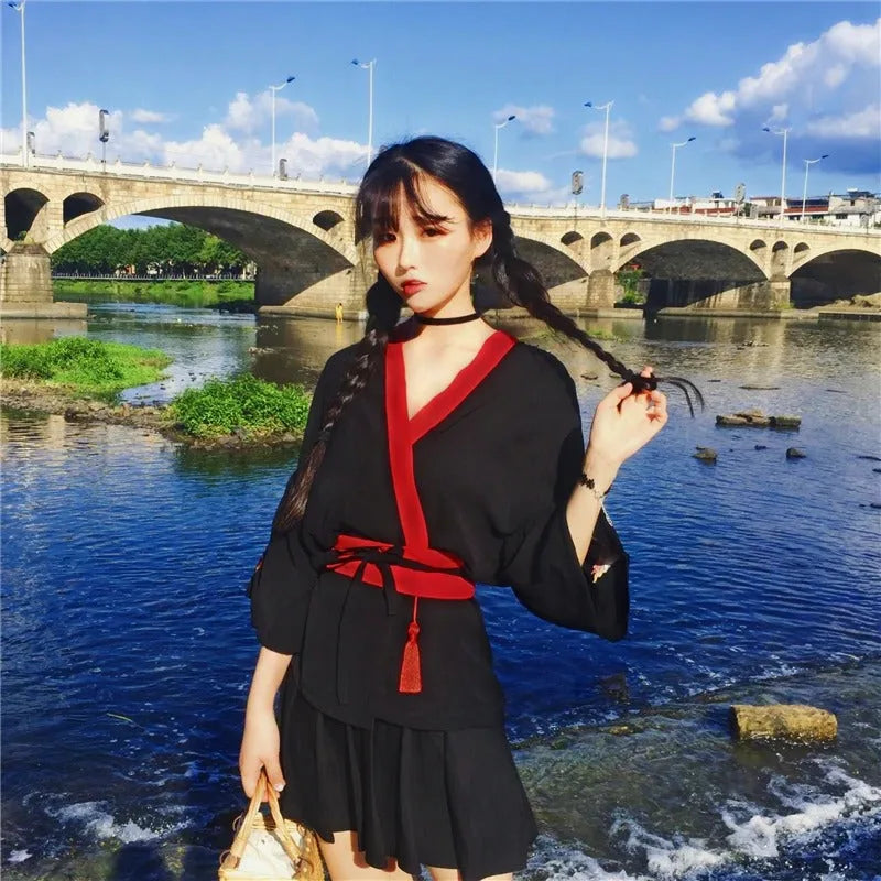 Stylowe czarne kimono damskie z motywem lisa kitsune i czerwonym pasem, prezentowane nad rzeką z mostem w tle.