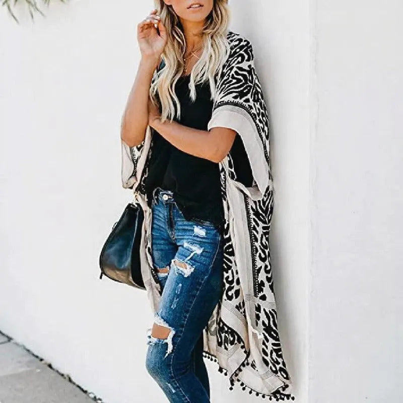 Stylowe kimono plażowe w czarno-białe wzory, z wykończeniem z pomponów, prezentowane z boku na modelce.