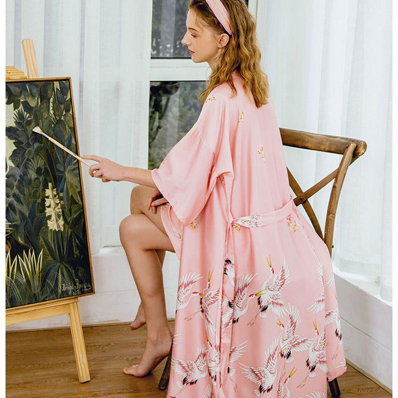 Kobieta w komfortowym różowym szlafroku kimono z żurawiami, siedząca i oddająca się pasji malowania.