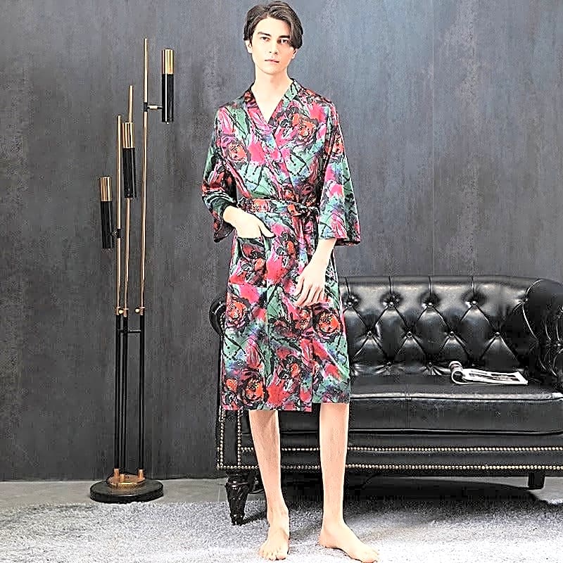 Elegancki satynowy szlafrok męski w stylu kimono, z wyrazistym wzorem czerwonych kwiatów na zielonym tle, noszony przez modela w nowoczesnym salonie.