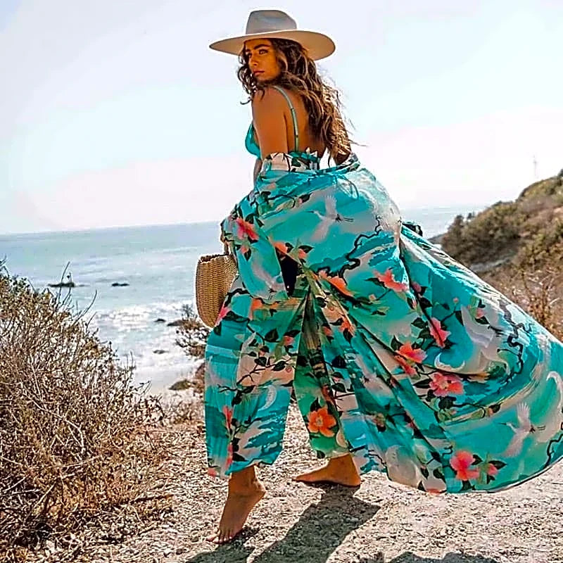 Turkusowa długa sukienka kimono z bawełny organicznej w japoński wzór z żurawiami, powiewająca na wietrze, noszona przez modelkę idącą po plaży.