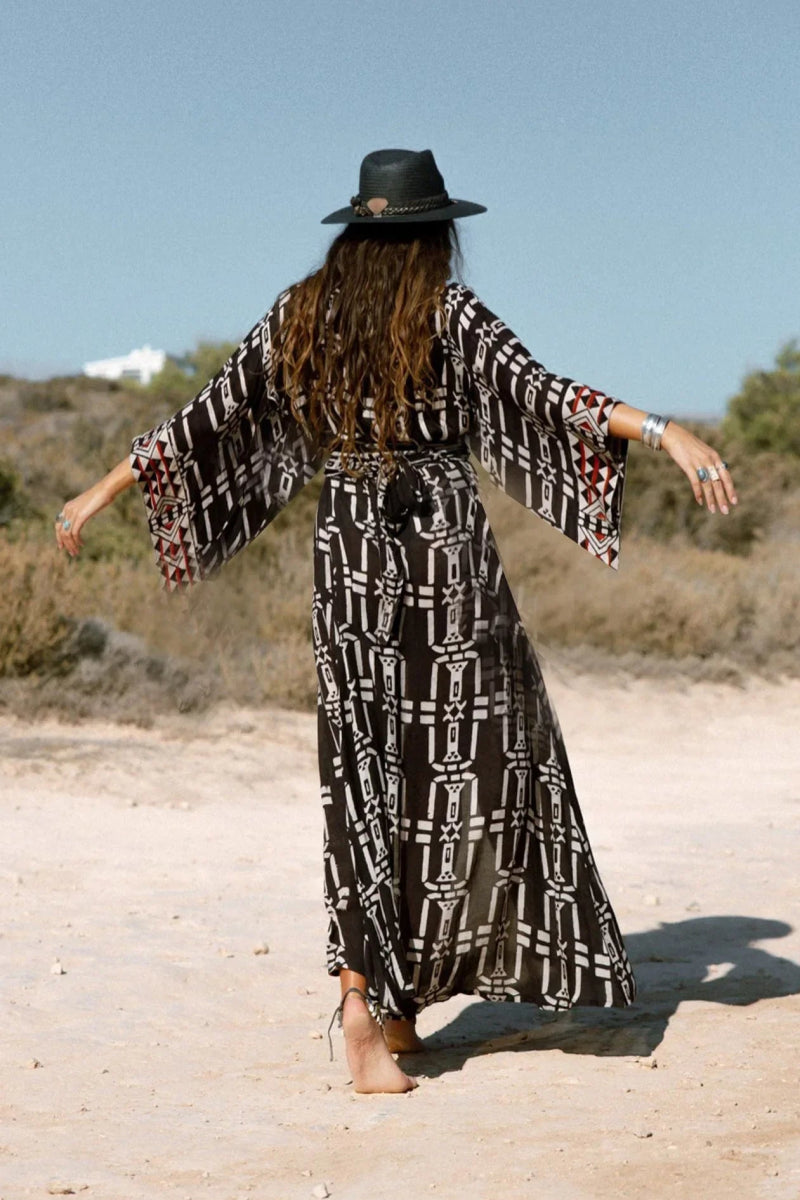 Tył długiej sukienki kimono w stylu boho, z szerokimi rękawami i unikalnym czarno-białym wzorem geometrycznym, widok z tyłu.